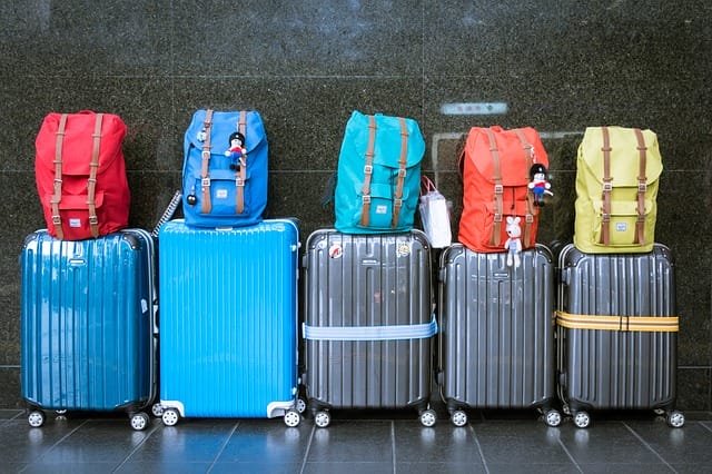 Five suitcases and bags lined against a wall.