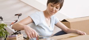 a woman taping a cardboard box in her room