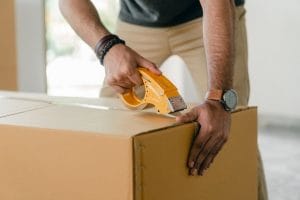 A man closing a moving box with duct tape.