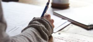 a woman writing things down with paper all over the tabel to depict the process of planning before packing your kitchen for a move