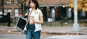 a woman carring a cat across the street in a pet carrier