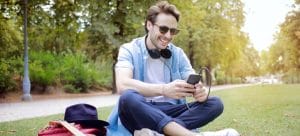 a man sitting on grass while using his smartphone and researching about mesquite nv vs henderson nv